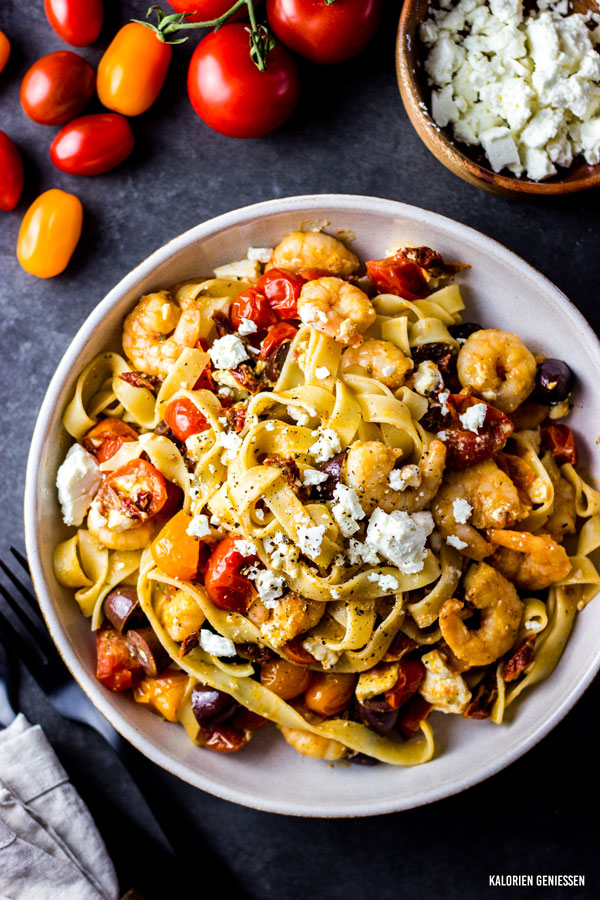 Kalorienarmes Rezept für Nudeln mit Schafskäse Feta und Garnelen, kombiniert mit getrockneten Tomaten und leckeren Kalamata-Oliven. Schnell in 20 Minuten in der Pfanne gemacht und ein tolles Gericht für den Feierabend oder Mittagspause. Statt Garnelen passt auch Hähnchen oder Tofu. Rezepte zum Abnehmen. - kaloriengeniessen.de #pasta #nudeln #spaghetti #feta #shrimp #schrimp #schafkäse #schafskäse #tomato #abendessen #kalorien